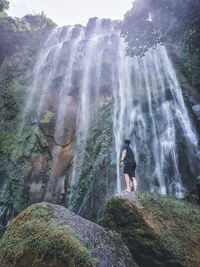 Full length of woman standing on rock against waterfall