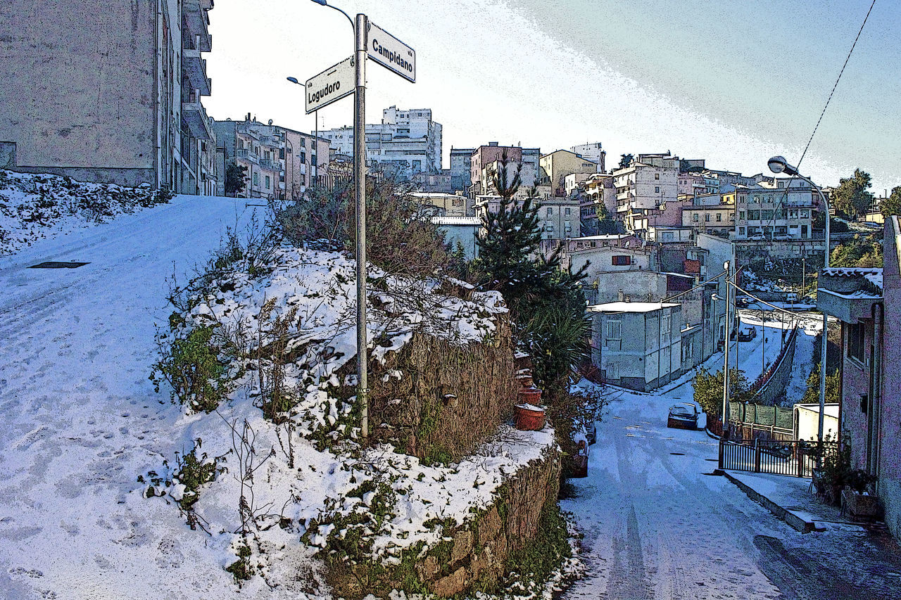 SNOW COVERED STREET BY BUILDINGS AGAINST SKY