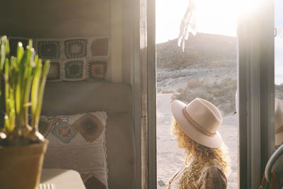 Rear view of woman looking through window at home