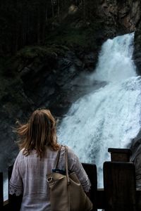 Rear view of woman looking at waterfall in forest