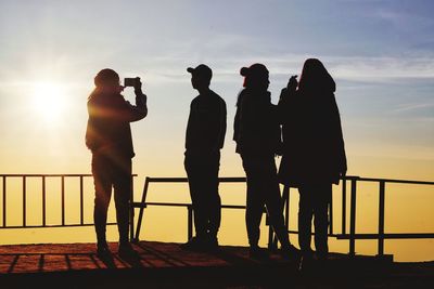 Silhouette people standing by railing against sky during sunset