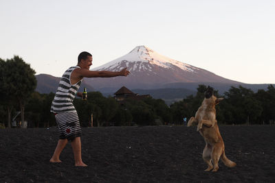 Full length of man playing with dog against mountain 