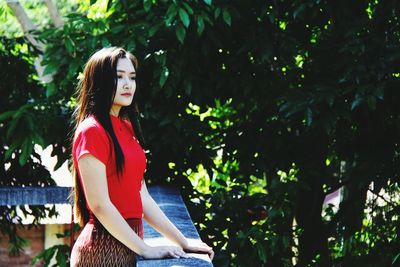 Young woman looking away while sitting on tree