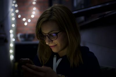 Young woman using mobile phone at home during night