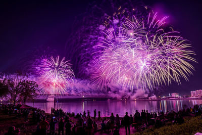 People looking at illuminated firework display over river at night