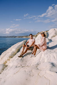 Woman sitting on beach by sea against sky