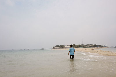 Rear view of men at beach against sky