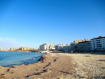 City buildings by sea against clear blue sky