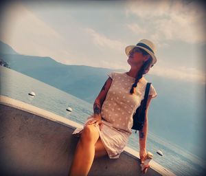 Young woman sitting on wood against sea against sky