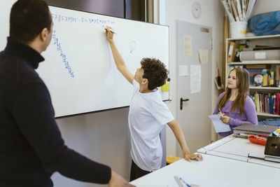 Schoolboy writing on whiteboard with teacher in classroom