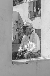 Senior man wearing hat and eyeglasses while sitting on chair seen through window