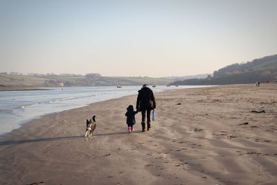 Rear view of woman with girl walking on sand at beach