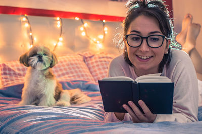 Smiling woman reading book on bed at home