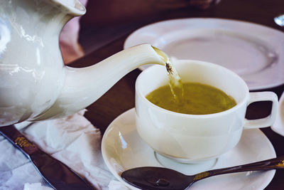 Cropped image of teapot pouring tea in cup on table