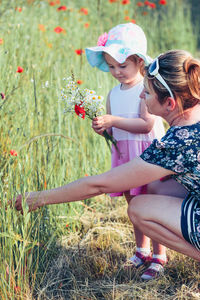 Girl holding flower by mother on grass