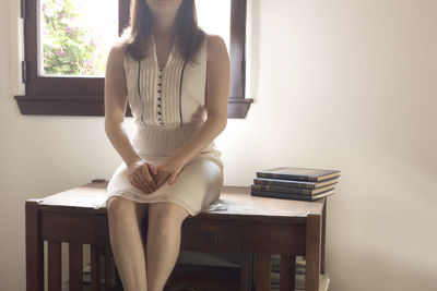 Midsection of young woman sitting on table at home