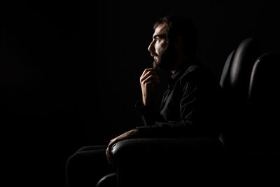 Man looking away while sitting against black background