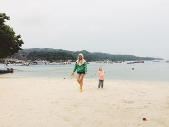 Full length of mother and daughter walking at beach against sky