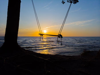 Silhouette sailboat on beach against sky during sunset