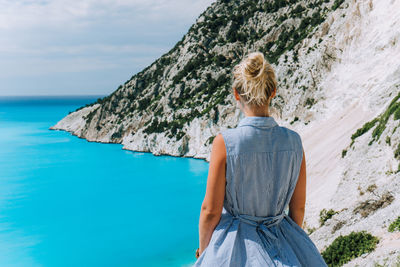 Rear view of woman standing on rock against sea