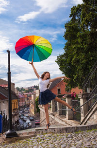 Woman standing on umbrella against sky in city