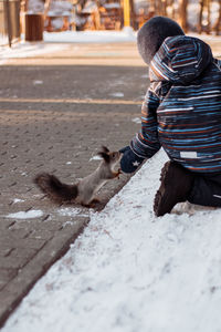 Rear view of girl playing with squirrel on snowy land
