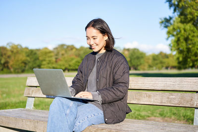 Young woman using laptop while sitting on bench at park