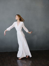 Young woman looking away while standing on floor against wall