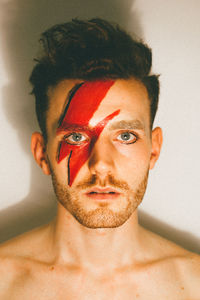 Close-up portrait of young man with red face paint while standing against wall