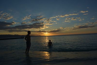 Silhouette people standing on beach against sky during sunset