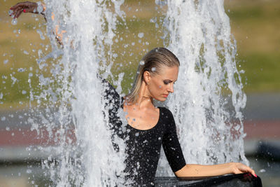 Beautiful woman with hand raised standing against fountain