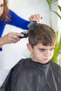 Angry boy getting haircut at home with scissors