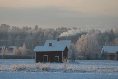 Houses on snow covered field against trees