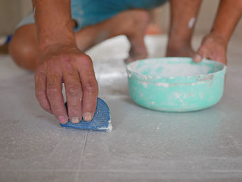 Low section of man applying cement on tiled floor