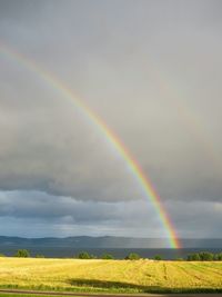 Rainbow over field against cloudy sky