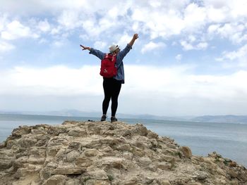 Rear view of woman standing on rock at beach against sky