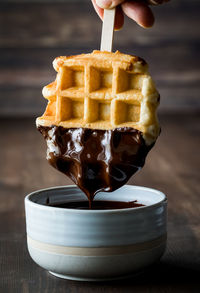 A waffle being dipped into melted chocolate and dripping into a bowl.