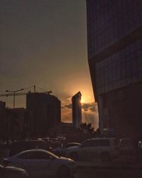 Cars on street by buildings against sky during sunset