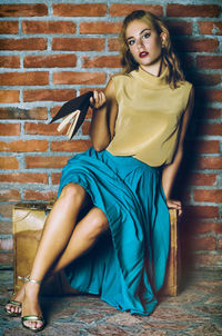 Portrait of young woman sitting on brick wall