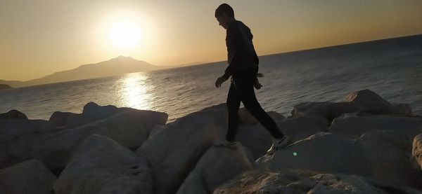 Full length of man on rocks at beach during sunset