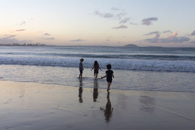 Children on beach against sky during sunset