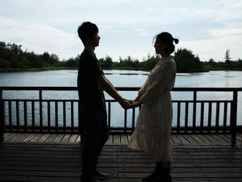 Side view of couple holding hands while standing against sky