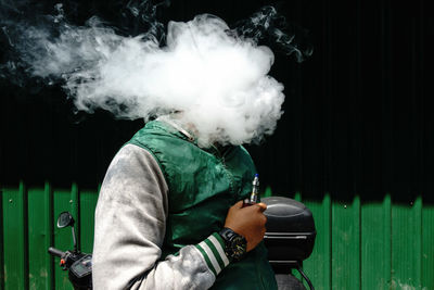 Man holding electronic cigarette while face covered with smoke