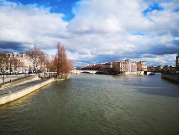 Arch bridge over river amidst buildings in city against sky