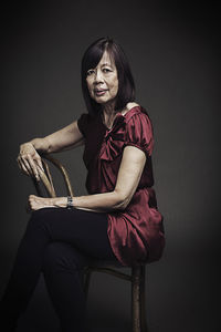Portrait of senior female sitting on chair against black background