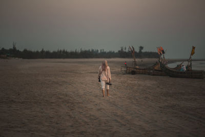 Rear view of a young muslim woman walking on the beach wearing a hijab during sunset