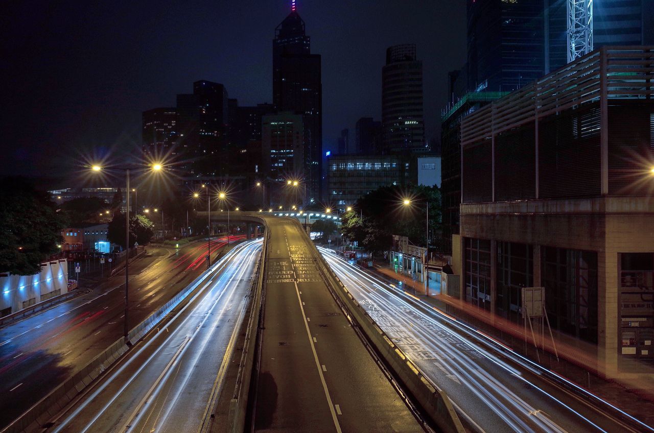 city, building exterior, illuminated, architecture, built structure, transportation, night, skyscraper, long exposure, road, city life, street, light trail, city street, speed, motion, the way forward, cityscape, office building, high angle view