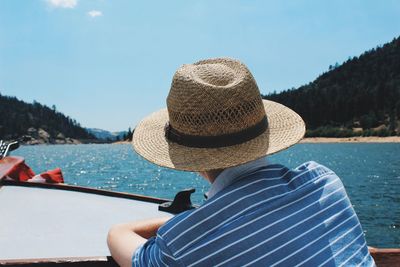 Rear view of man sitting on boat in sea against sky