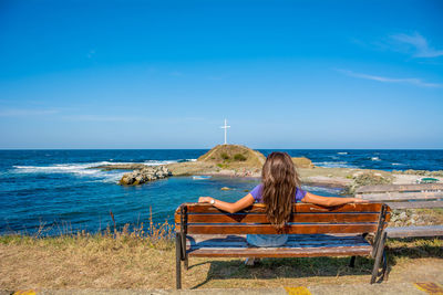 Rear view of woman sitting on bench against sea at beach