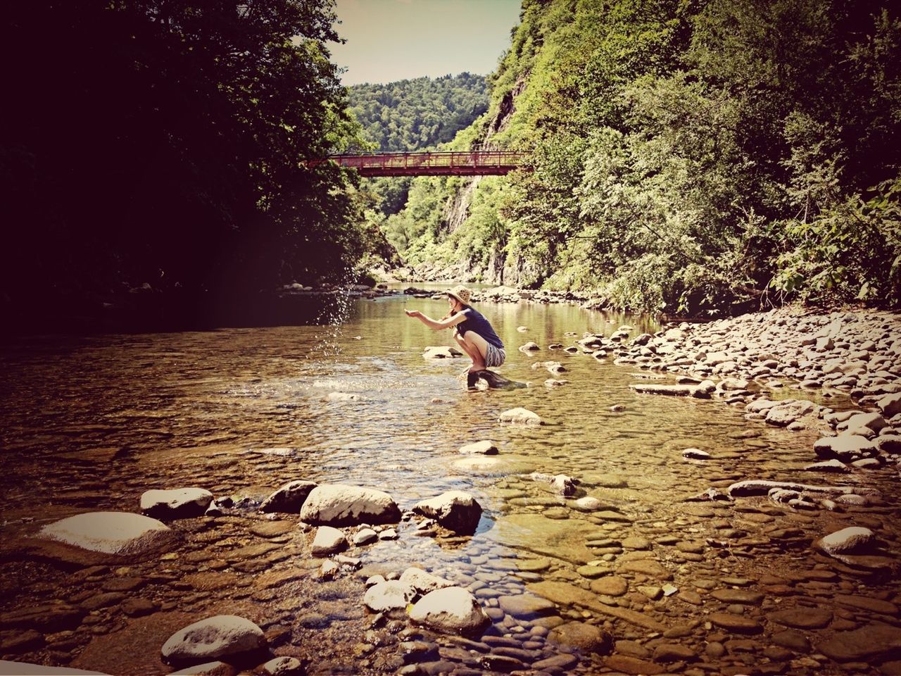 water, tree, lifestyles, leisure activity, built structure, day, sunlight, nature, rock - object, outdoors, river, full length, stone - object, park - man made space, architecture, tranquility, person, incidental people